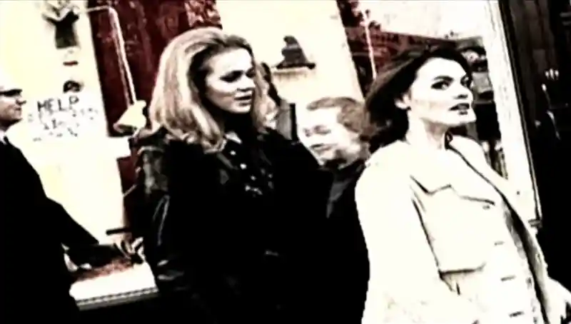 Street shot with two women walking past a shopfront, with a "Help!" sign in the background