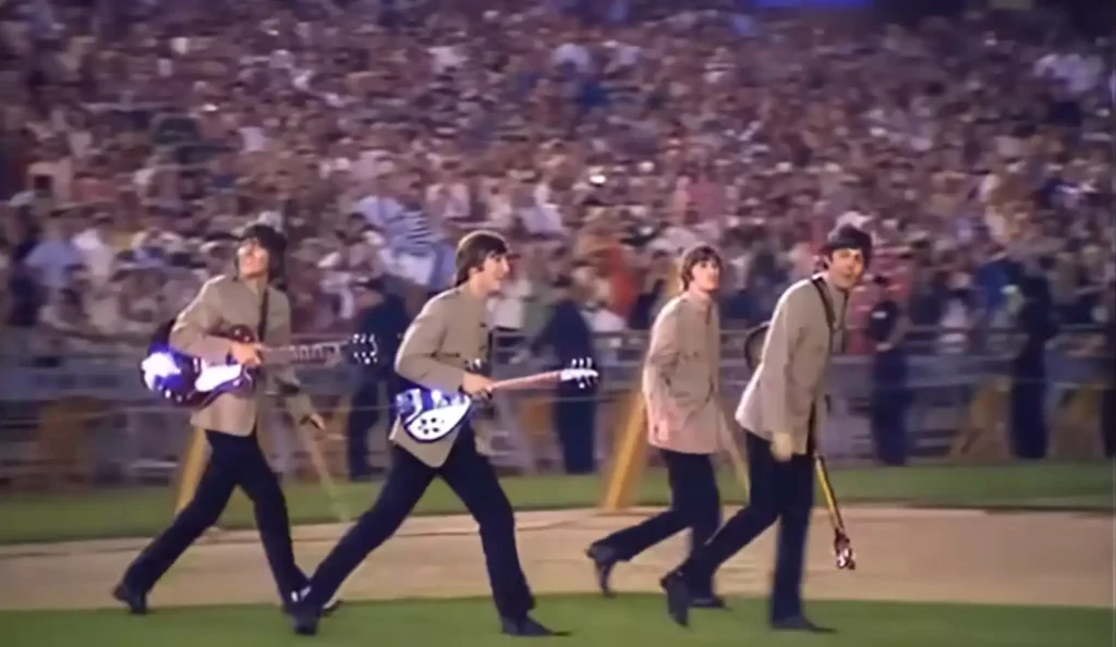 The Beatles walking toward the stage at Shea Stadium in 1965, taken from the official television documentary.